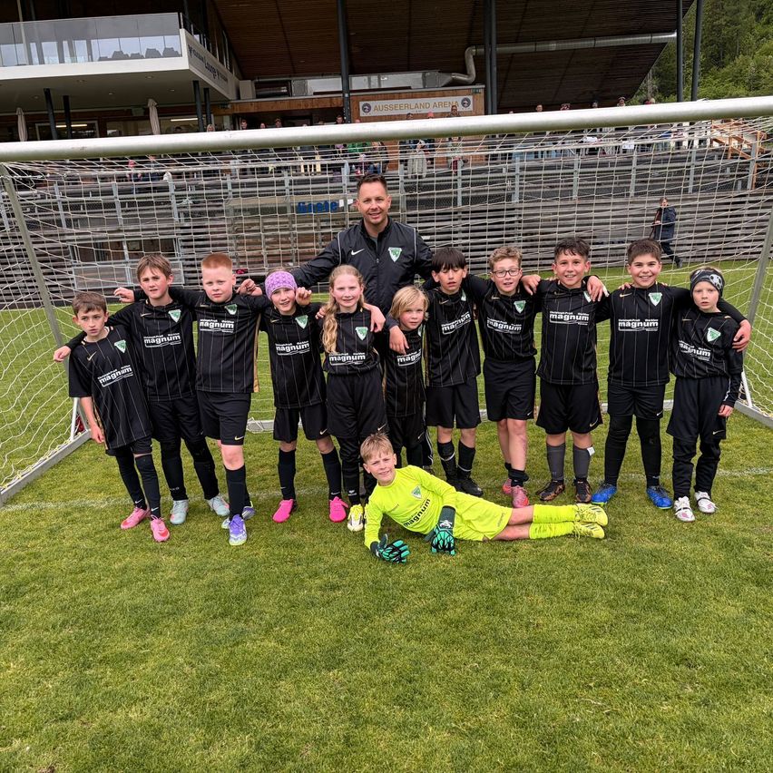 Eine Fußballmannschaft mit jungen Spielern und einem Trainer posiert für ein Foto vor einem Tor. Sie tragen schwarze und gelbe Trikots.