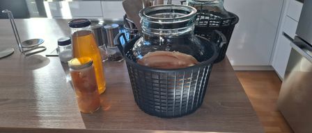 Eine Küchentheke mit einem schwarzen Korb, der einen Glaskrug mit Flüssigkeit enthält. Zwei weitere Glasgefäße, ein Pfefferstreuer und ein Salzstreuer stehen auf der Theke.