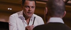 Leonardo DiCaprio, eine Feder in der Hand, scheint sich in einem ernsthaften Gespräch mit einem anderen Mann in einem schwarzen Anzug zu befinden.