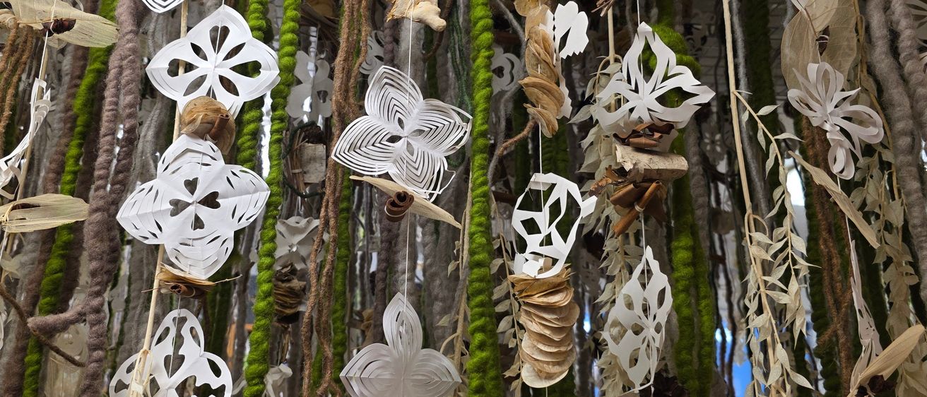 Eine Nahaufnahme einer komplexen Kunstinstallation mit weißen Papierausschnitten und grünem Moos, die von einer Decke hängen und Schmetterlinge und Blätter ähneln.