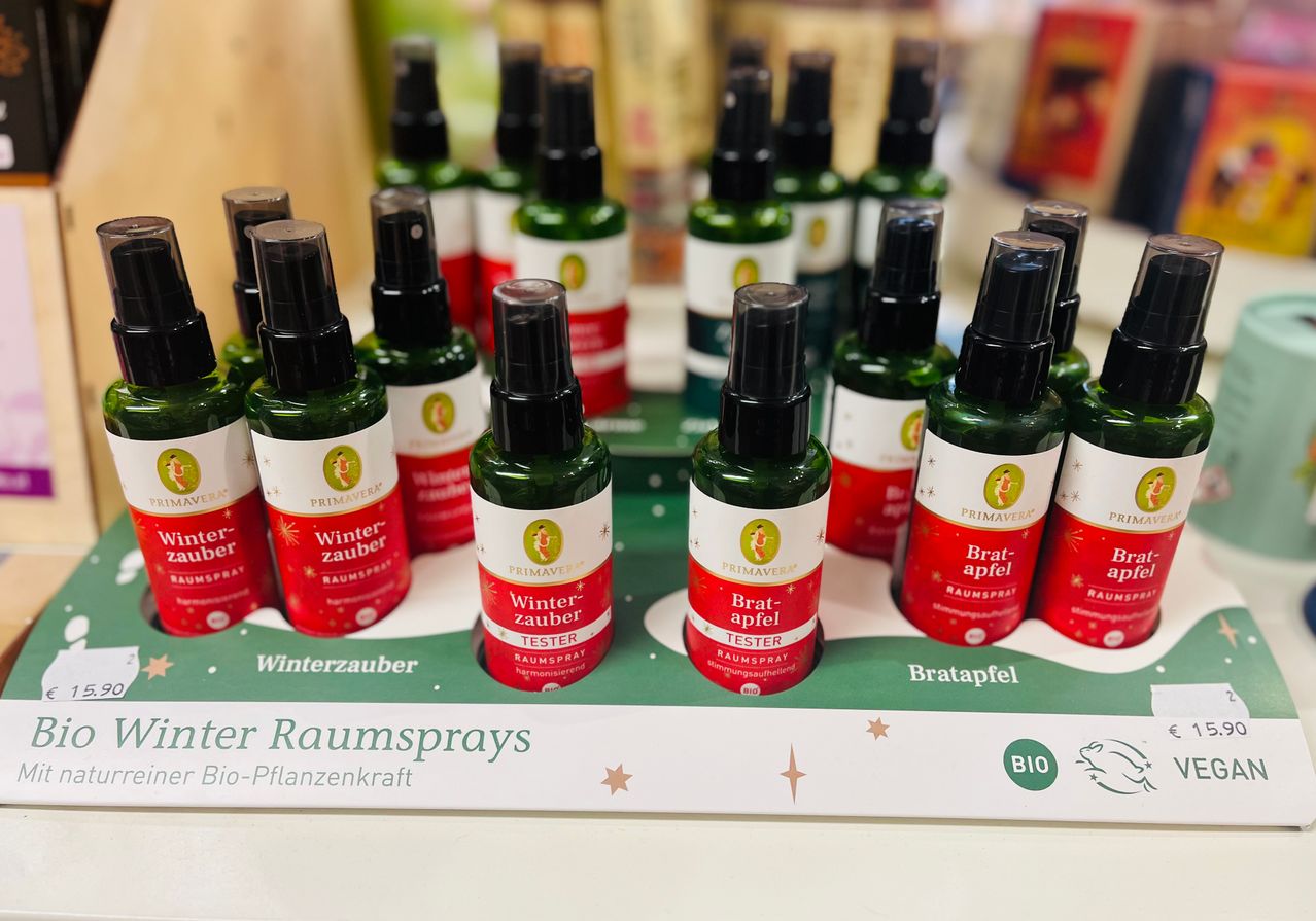 Eine Ausstellung von Primavera Winterzauber und Bratapfel Lufterfrischern in grünen Flaschen mit schwarzen Kappen auf einem Regal.