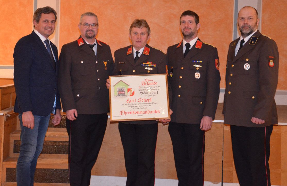 Fünf Männer in Uniform stehen zusammen; einer hält eine Plakette und lächelt. Die Plakette trägt die Aufschrift 'Ehrenurkunde' und 'Karl Schopf'. Dahinter ist eine Treppe zu sehen.
