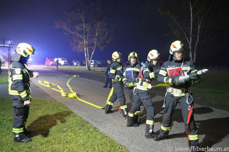 Eine Gruppe von Feuerwehrleuten in voller Ausrüstung steht bei Nacht am Straßenrand. Sie halten eine Feuerwehrhose.