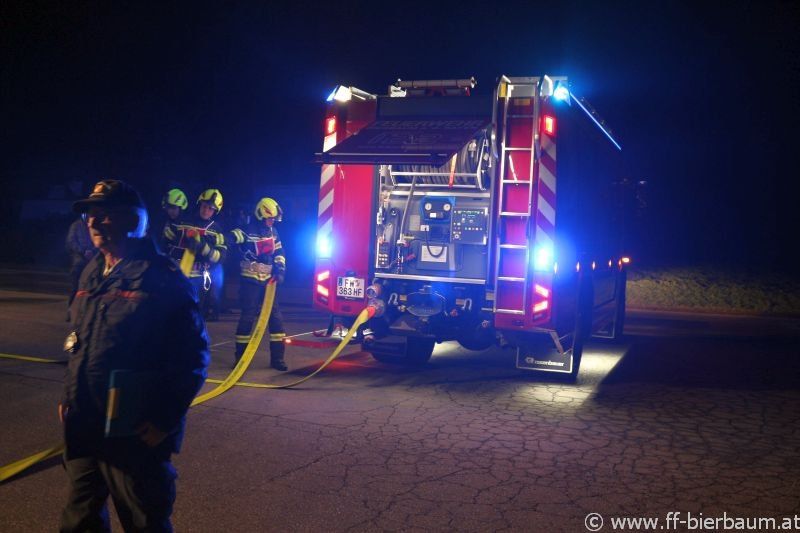 Feuerwehrleute bereiten einen Feuerwehrwagen mit blinkenden Lichtern auf einer Straße bei Nacht vor.