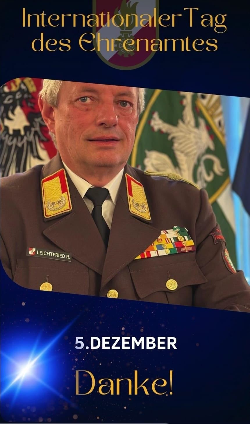 Ein Mann in Uniform steht vor einer Fahne. Er trägt eine Krawatte und hat Medaillen auf der Brust.