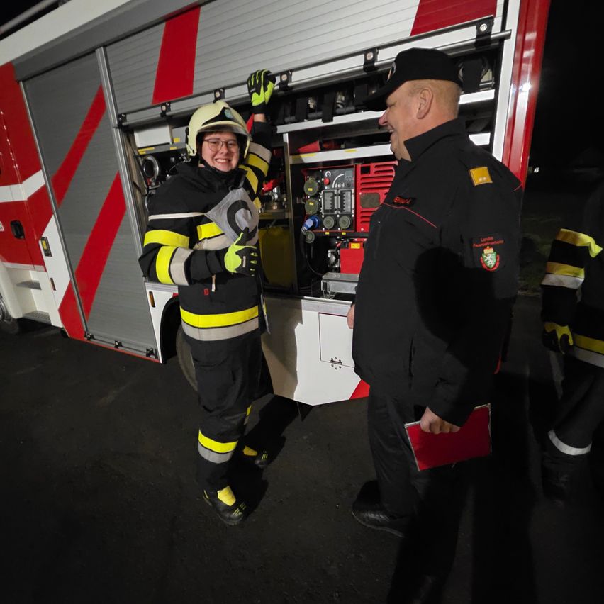A firefighter in full gear interacts with a colleague, both smiling under the night sky.