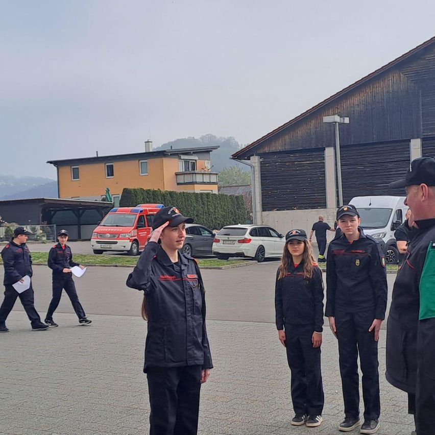 A group of individuals in uniforms are standing in front of a building with some cars parked in the background.