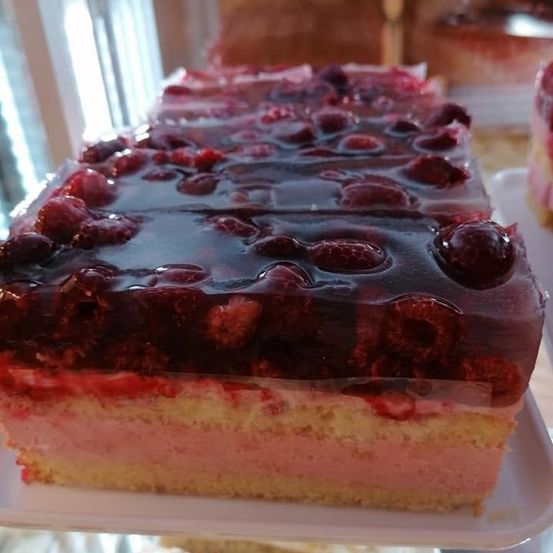 Ein Stück Kuchen mit einer Schicht Himbeergelee obenauf, auf einem weißen Teller präsentiert.