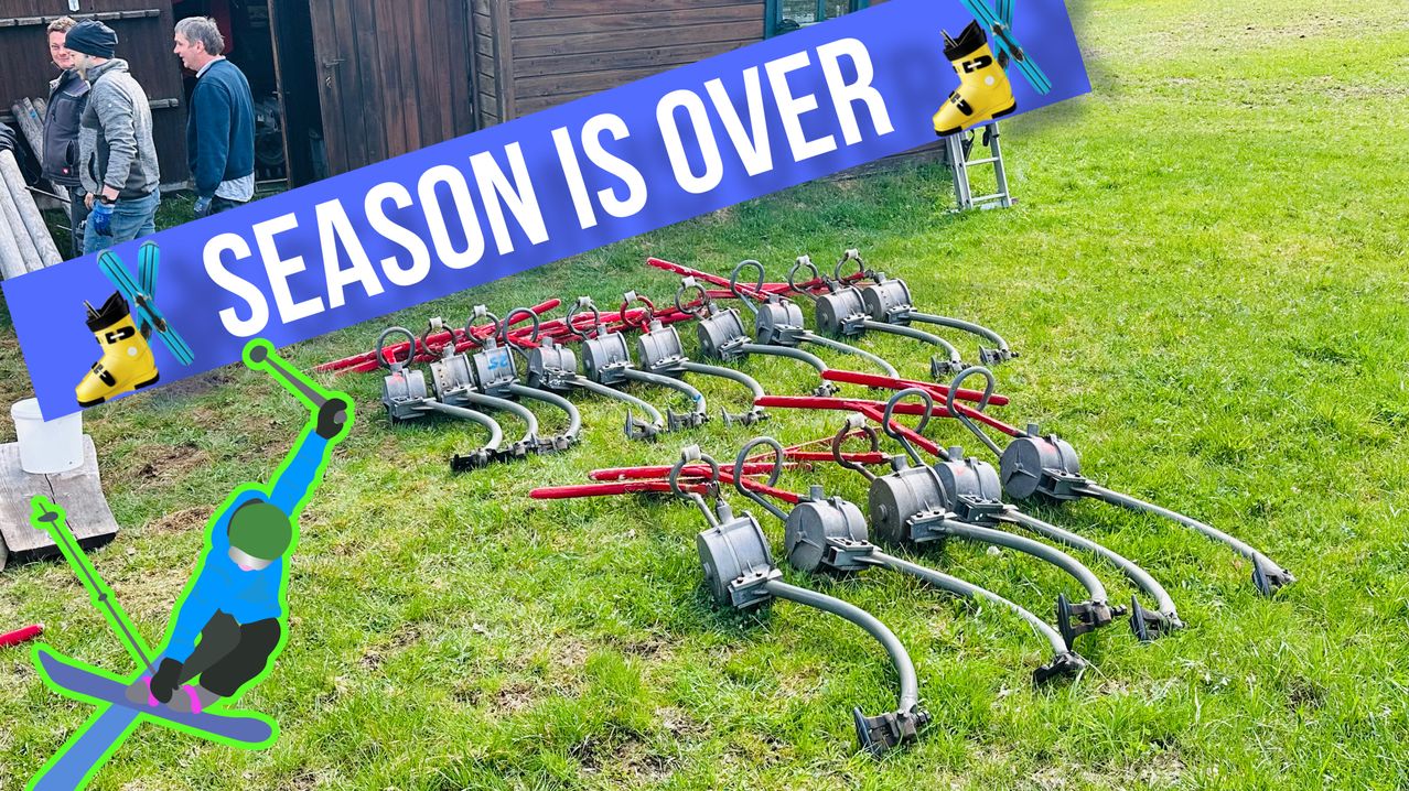 A blue sign with white text reading 'SEASON IS OVER' hangs above rows of red and gray objects resembling irrigation sprinklers on a grassy field.