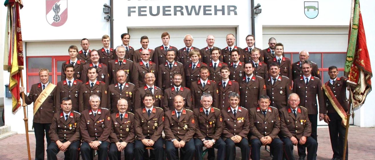 Eine Gruppe von Männern in braunen Uniformen posiert für ein Foto vor einem Gebäude mit der Aufschrift Freiwillige Feuerwehr.