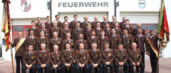 Eine Gruppe von Männern in braunen Uniformen posiert für ein Foto vor einem Gebäude mit der Aufschrift Freiwillige Feuerwehr.