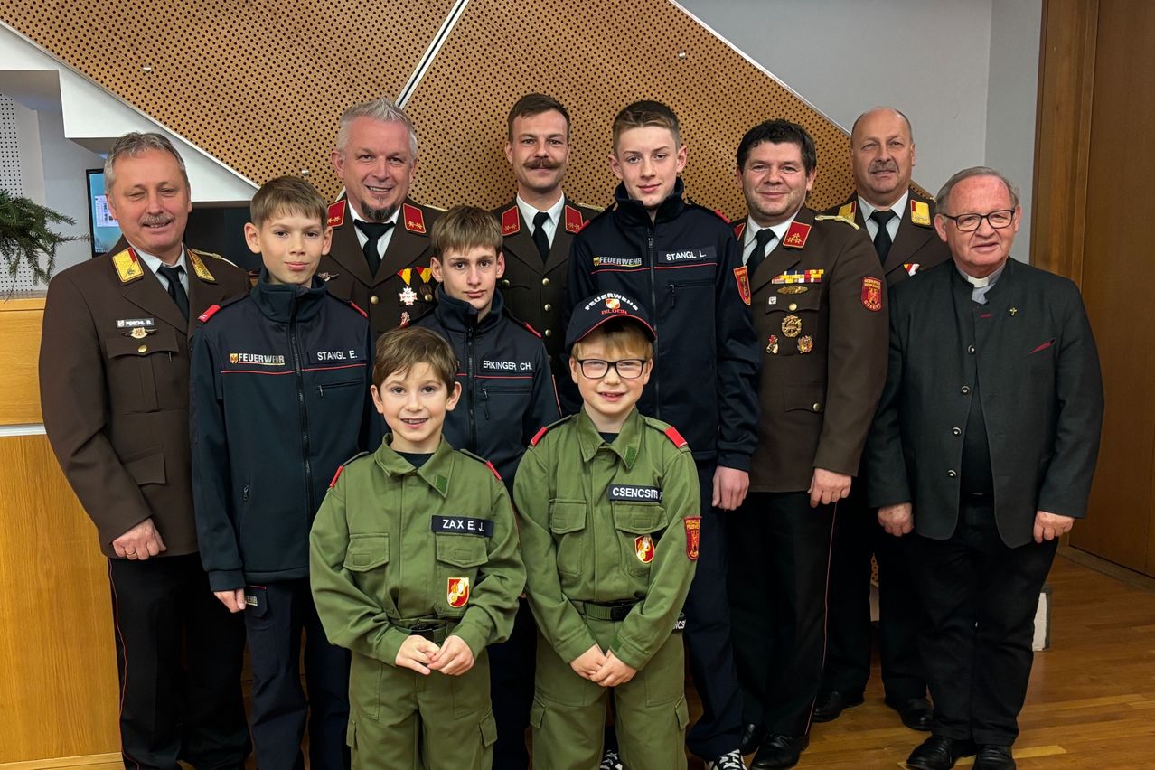Mehrere Personen in Uniformen, darunter zwei Jungen in grünen Militäruniformen, posieren für ein Gruppenfoto. Dahinter stehen mehrere Männer in Militäruniformen.