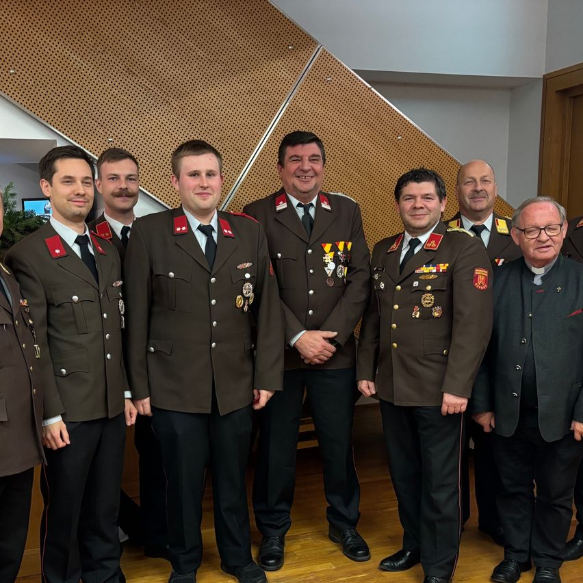 Eine Gruppe von Männern in Militäruniformen steht für ein Foto zusammen, einer trägt eine Brille und ein Geistlicher in einem schwarzen Anzug.