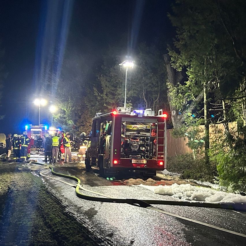 A fire truck is parked on the road with its lights on, with firefighters standing around. A hose is on the ground. Streetlights are on, and a building is nearby.