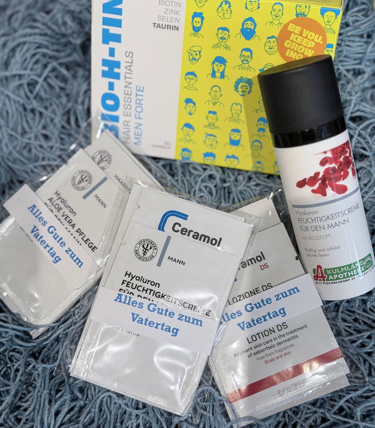 A collection of skin care products including lotion, serum, and sachets on a blue surface. The products are labeled with text in German.