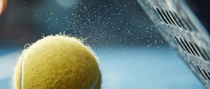 Ein Tennisball trifft auf den blauen Platz und erzeugt eine Staubwolke. Der Ball ist gelb mit einer weißen Linie.