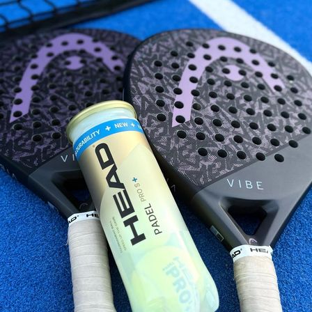 Zwei Vibe Schläger und eine HEAD Padel Pro Dose mit weißer und gelber Aufschrift auf einem blauen Platz.