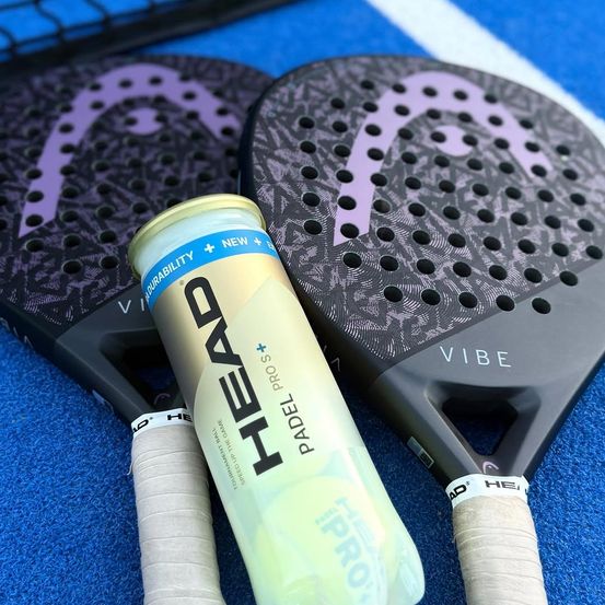 Zwei Vibe Schläger und eine HEAD Padel Pro Dose mit weißer und gelber Aufschrift auf einem blauen Platz.