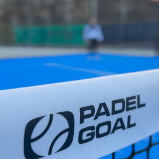 Ein verschwommener Blick auf eine Person auf einem blauen Padel-Court mit einem weißen Netz. Das Netz hat das Logo 'Padel Goal'.