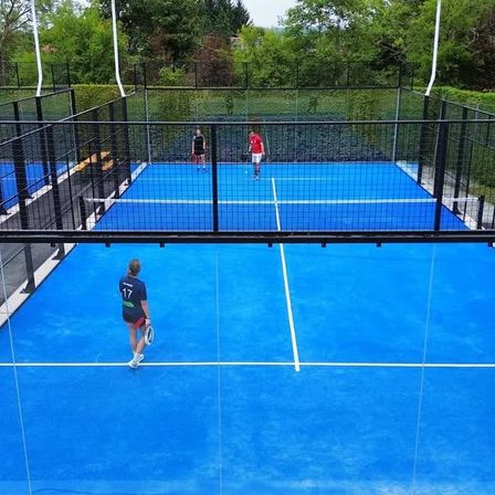 Eine Gruppe von Menschen spielt Tennis auf einem blauen Platz, umgeben von einem schwarzen Zaun. Zwei sind in Aktion, während zwei an den Seitenlinien stehen.