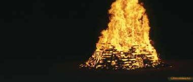 Ein Lagerfeuer brennt bei Nacht. Der Mond am Himmel wirft ein sanftes Licht auf das Feuer.