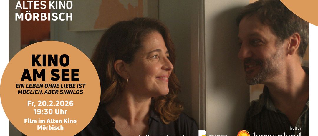 Eine lächelnde Frau in einem schwarzen Shirt schaut jemanden auf ihrer rechten Seite an. Hinter ihr befindet sich eine Wand mit etwas Text, und eine andere Person ist auf der rechten Seite. Das Bild hat einen Wasserzeichen auf der unteren rechten Seite.