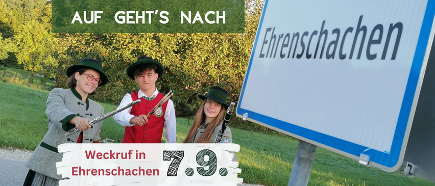 Drei Personen in traditioneller Kleidung posieren für ein Foto vor einem Schild, das 'Ehrenschachen' und ein Datum von 7.9 anzeigt. Der Text 'Auf geht's nach' ist darüber angebracht.