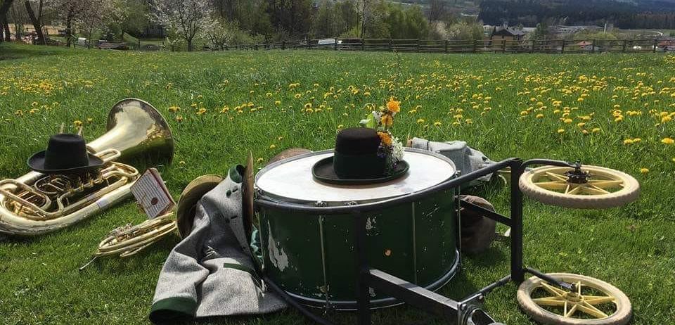 Eine Trommel mit Hut, Blumen und Uniform liegt in einer Wiese mit Löwenzahn und Bäumen im Hintergrund.