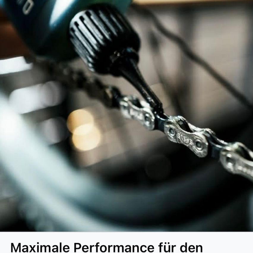 Eine Person benutzt ein schwarzes Werkzeug, um an einer Fahrradkette zu arbeiten. Die Kette ist silber mit sichtbaren Gliedern. Der Hintergrund ist unscharf mit einem Hauch von Gelb.