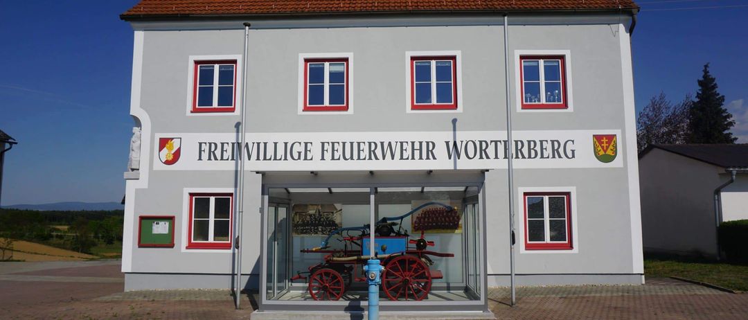 Ein Feuerwehrhaus mit einem historischen Pferdefuhrwerk, das vor dem Gebäude ausgestellt ist.