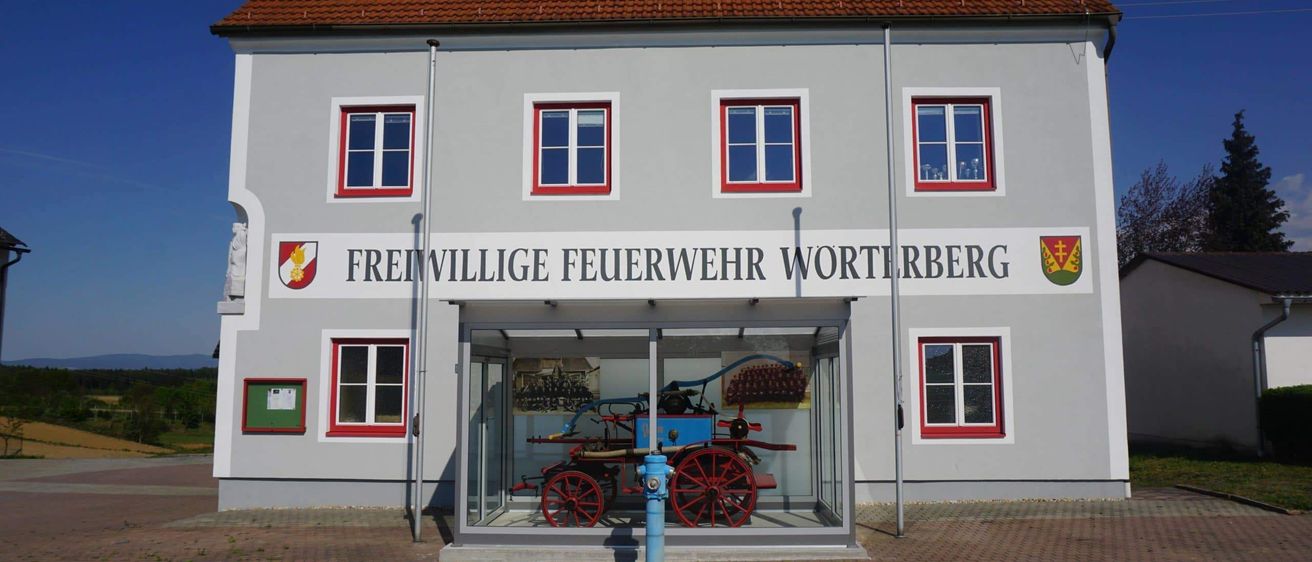 Ein Feuerwehrhaus mit einem historischen Pferdefuhrwerk, das vor dem Gebäude ausgestellt ist.