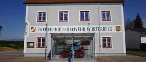 Ein Feuerwehrhaus mit einem historischen Pferdefuhrwerk, das vor dem Gebäude ausgestellt ist.