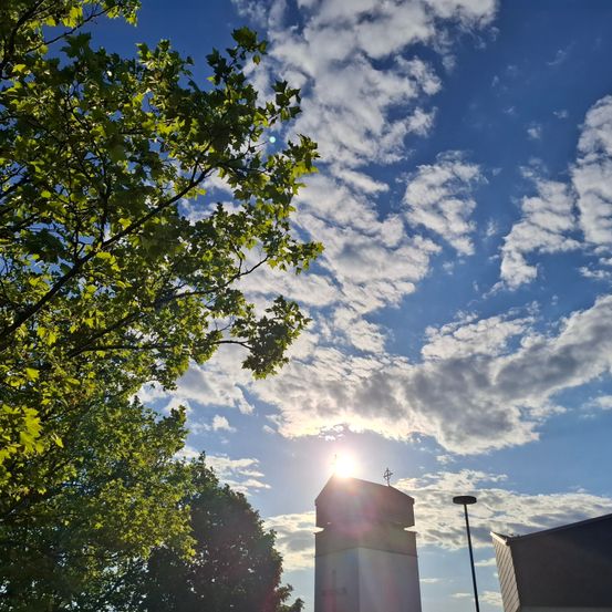 Ein sonniger Tag mit blauem Himmel voller Wolken, die Sonne scheint hell. Ein hoher Turm steht inmitten des Waldes.