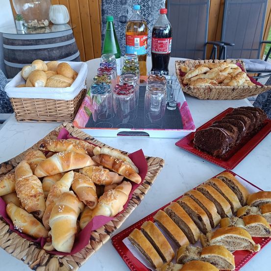 Ein Tisch mit verschiedenen Gebäckstücken, darunter Croissants, Brötchen und Scheiben Brot. Es gibt auch Getränke in Flaschen und Gläsern auf dem Tisch.