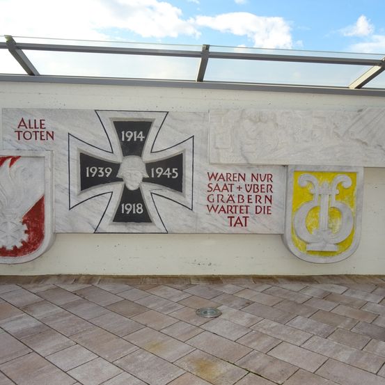 Eine Gedenkwand mit dem deutschen Eisernen Kreuz von 1914, 1939 und 1945, mit 'Alle Toten' und 'Waren nur Graber' darauf geschrieben.