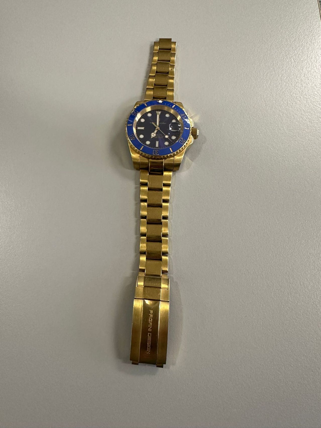 Eine goldfarbene Armbanduhr mit blauem Zifferblatt und weißer Sekundenzeiger. Die Uhr hat ein metallisches Armband.