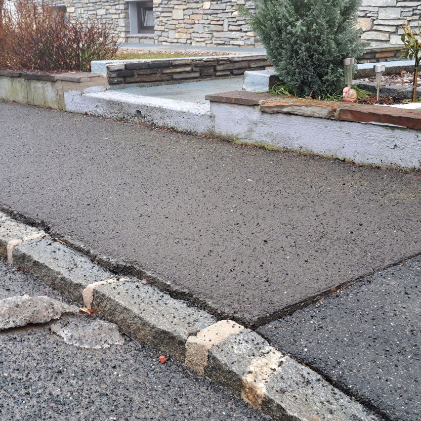 Ein gepflasterter Weg mit Bordstein, Steinmauer und Betonfläche in der Nähe eines Hauses.
