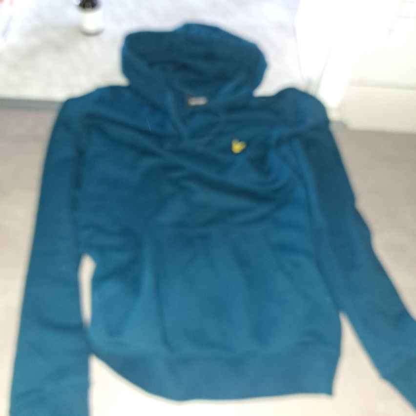 A teal hoodie with a yellow logo on the chest area is folded and placed on a white surface.