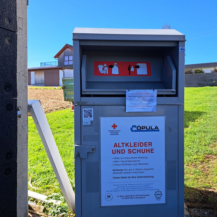 An outdoor clothing donation box with instructions on how to properly donate. The box is placed on a lawn, with houses and trees in the background.