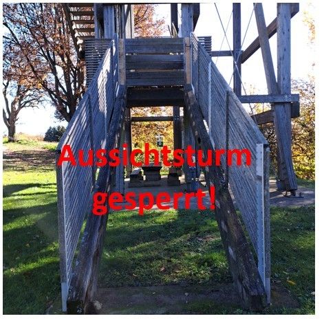 A view of a wooden lookout tower with the text 'Viewpoint closed due to storm' written in red. The tower is surrounded by a grassy field with trees.