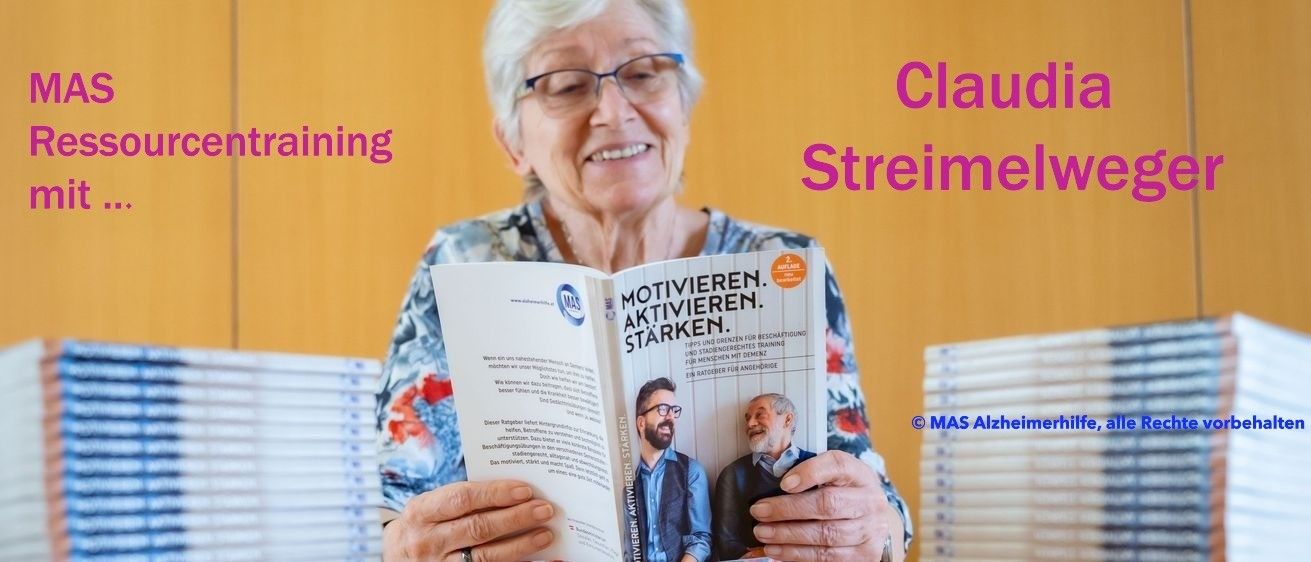 Eine ältere Frau lächelt, während sie ein Buch mit dem Titel 'Motivieren. Aktivieren. Stärken.' liest. Sie hält es in den Händen. Hinter ihr ist eine Wand mit Text zu sehen.