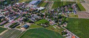 Luftaufnahme eines ländlichen Gebiets mit einem Stadtzentrum, umgeben von landwirtschaftlichen Feldern, darunter ein großes grünes Feld und ein kleines Industriegebiet.