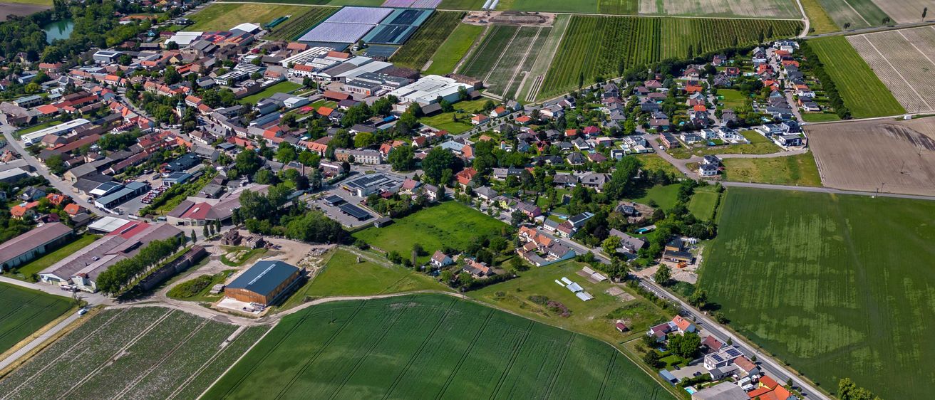 Luftaufnahme eines ländlichen Gebiets mit einem Stadtzentrum, umgeben von landwirtschaftlichen Feldern, darunter ein großes grünes Feld und ein kleines Industriegebiet.
