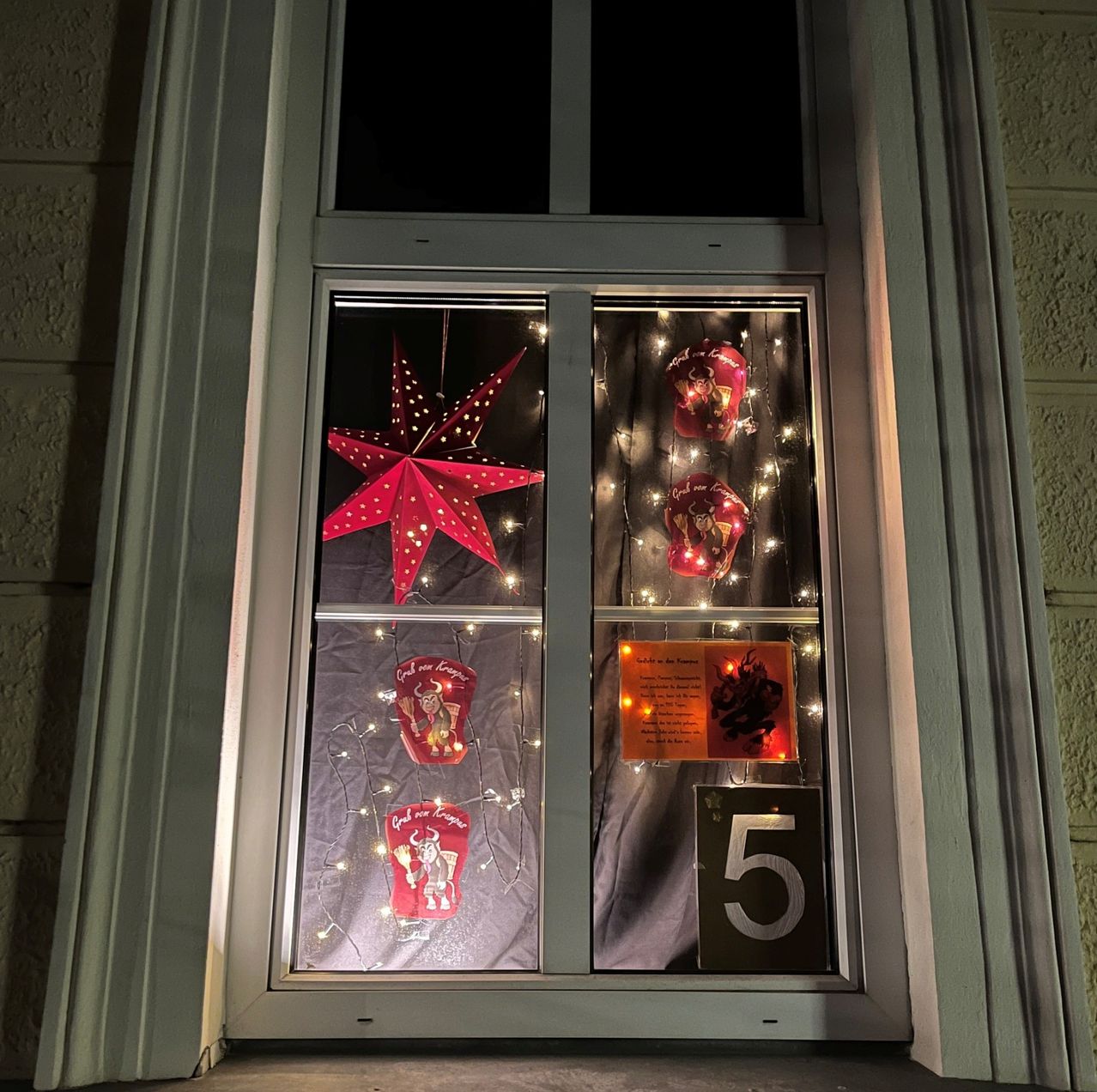 Ein Fenster zeigt eine festliche Szene mit einem roten Stern, brennenden Kerzen und Feiertagsdekorationen, zusammen mit der Nummer 5.