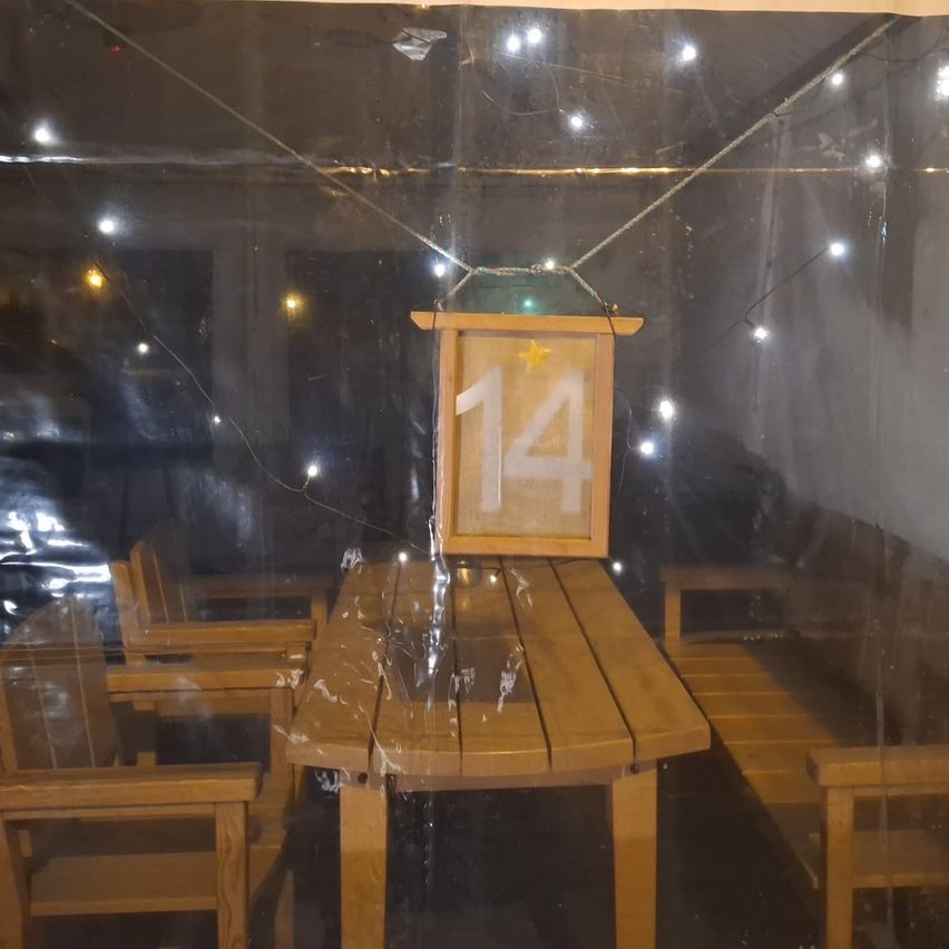 Ein Raum mit einem Holztisch und Stühlen ist mit Plastik bedeckt. Ein Schild mit der Nummer 14 hängt über dem Tisch. Der Raum ist schwach beleuchtet.