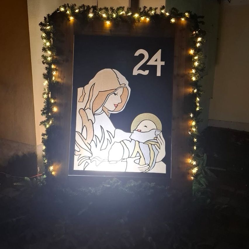 Ein beleuchteter Holzrahmen mit einem weihnachtlichen Bild einer Mutter und eines Kindes, umgeben von dekorativen Lichtern, zeigt die Nummer 24.