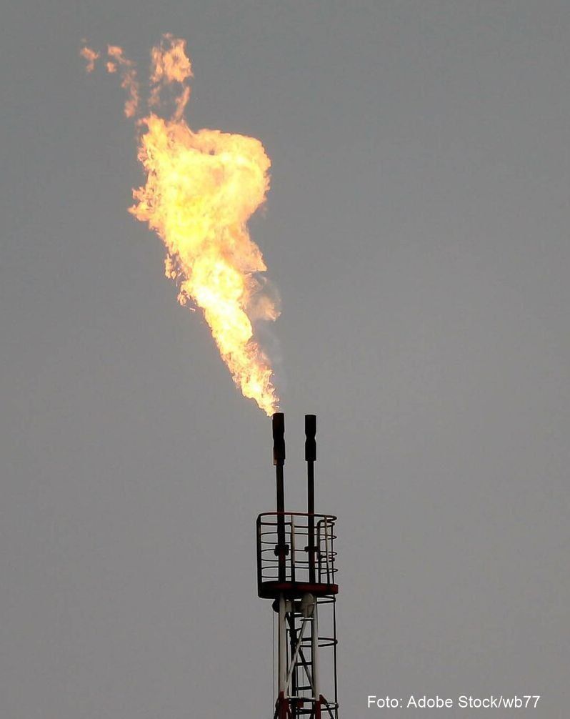 Ein Gasfackelturm gibt eine gelbe Flamme gegen einen grauen Hintergrund am Himmel ab.