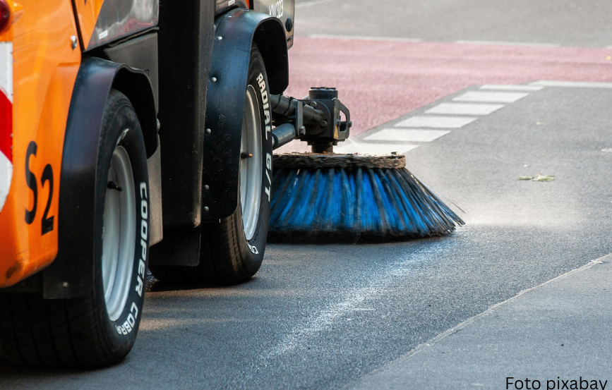 Ein Straßenkehrer mit orange und schwarzen Farben reinigt die Straße. Er hat einen blauen Besen und eine radiale Bereifung.