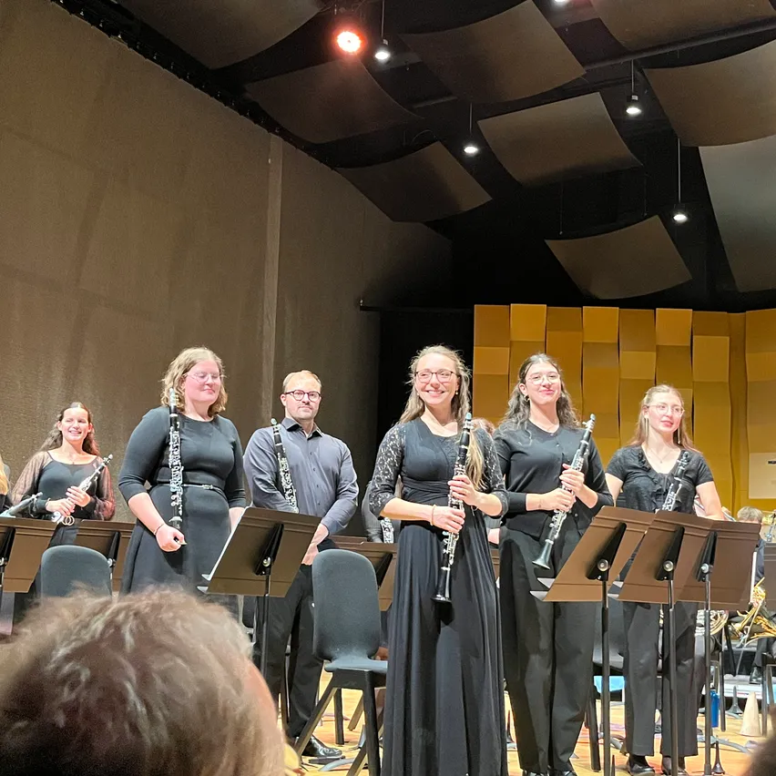 Eine Gruppe von Musikern in schwarzer Kleidung spielt auf der Bühne mit Klarinetten und anderen Instrumenten vor einem Publikum.