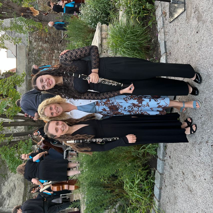 Eine Gruppe von Musikern, darunter drei Frauen, stehen und posieren für ein Foto. Die Frau in der Mitte hält eine Klarinette.